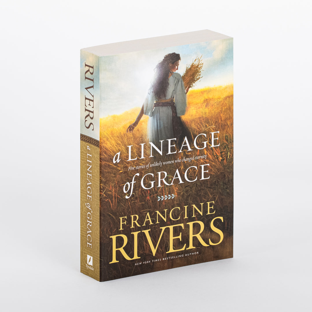 Paperback of A Lineage of Grace by Francine Rivers at a three-quarter angle, showing the front cover and spine on a white background. The cover shows a woman with long, dark wavy hair in a pale blue-gray robe walking through a golden wheat field, seen from behind, carrying wheat stalks under a blue sky. White serif title text reads A Lineage of Grace: Five stories of unlikely women who changed eternity, with the author's name in gold and a New York Times Bestselling Author banner below.