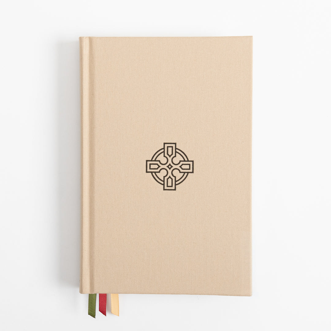 Straight-on view of the tan linen hardcover, its cover blank except for a black embossed Celtic cross centered on the front. Three ribbon markers - olive green, red, and gold - hang from the bottom edge.