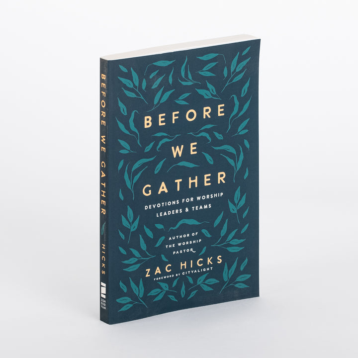 Angled three-quarter view of the paperback Before We Gather: Devotions for Worship Leaders and Teams by Zac Hicks, showing the dark teal cover with a gold and teal leaf-vine pattern, cream title lettering, and the matching spine text.
