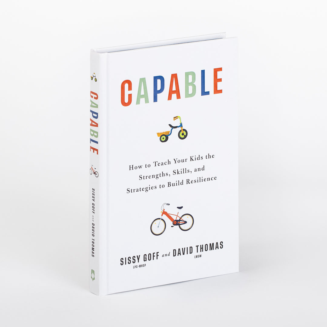 Hardcover book Capable by Sissy Goff and David Thomas shown at an angle, revealing both the white front cover and spine. Colorful title letters sit above a small tricycle illustration, with the subtitle How to Teach Your Kids the Strengths, Skills, and Strategies to Build Resilience and a bicycle illustration above the authors' names.