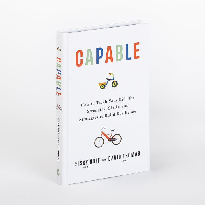 Hardcover book Capable by Sissy Goff and David Thomas shown at an angle, revealing both the white front cover and spine. Colorful title letters sit above a small tricycle illustration, with the subtitle How to Teach Your Kids the Strengths, Skills, and Strategies to Build Resilience and a bicycle illustration above the authors&