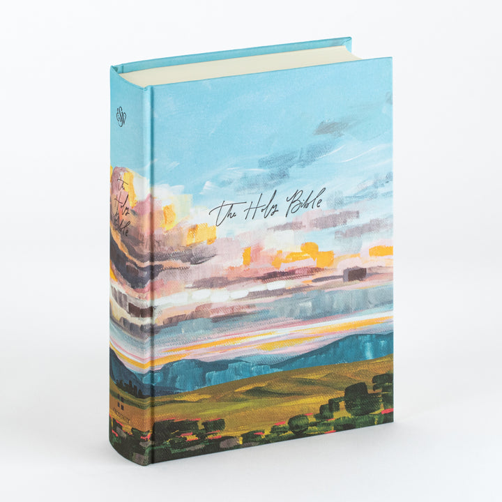 Cloth-over-board Bible cover with a painted sunset landscape: pale blue sky brushed with pink, orange, and white clouds over teal hills and a golden field dotted with dark green trees. &