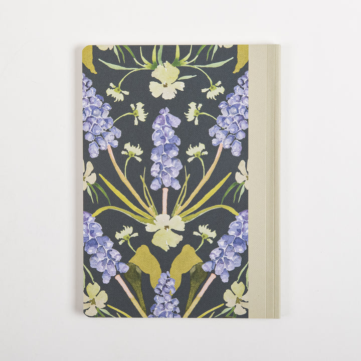 Back cover of the Forgiveness prayer journal, displaying the same symmetrical watercolor pattern of purple grape hyacinth spikes and pale yellow wildflowers on a dark green ground, with no text and the cream fabric spine visible along the right edge.