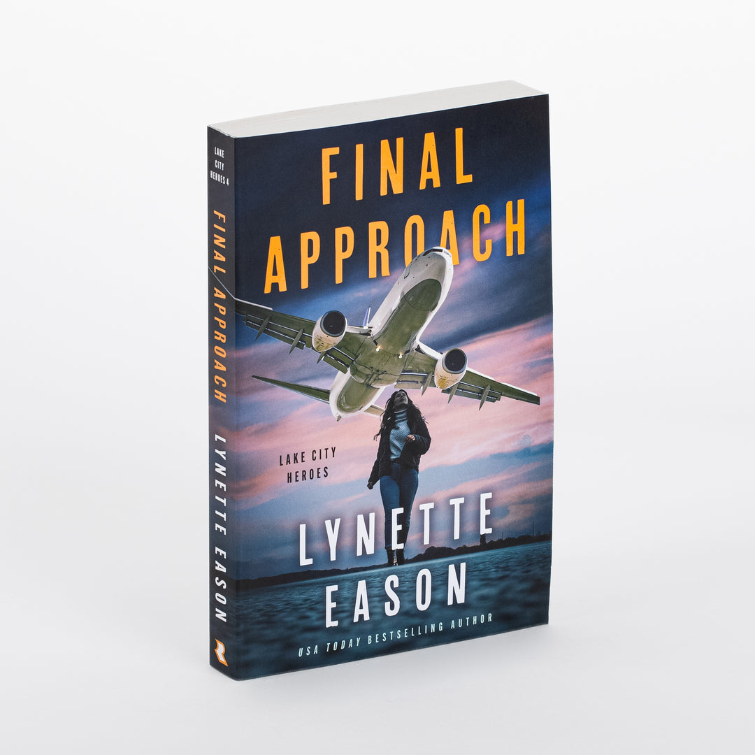 Paperback cover of 'Final Approach' by Lynette Eason shown at an angle, revealing spine and front: a jet airplane flying low over a woman walking near water at dusk, orange title text, and 'Lake City Heroes' series label.