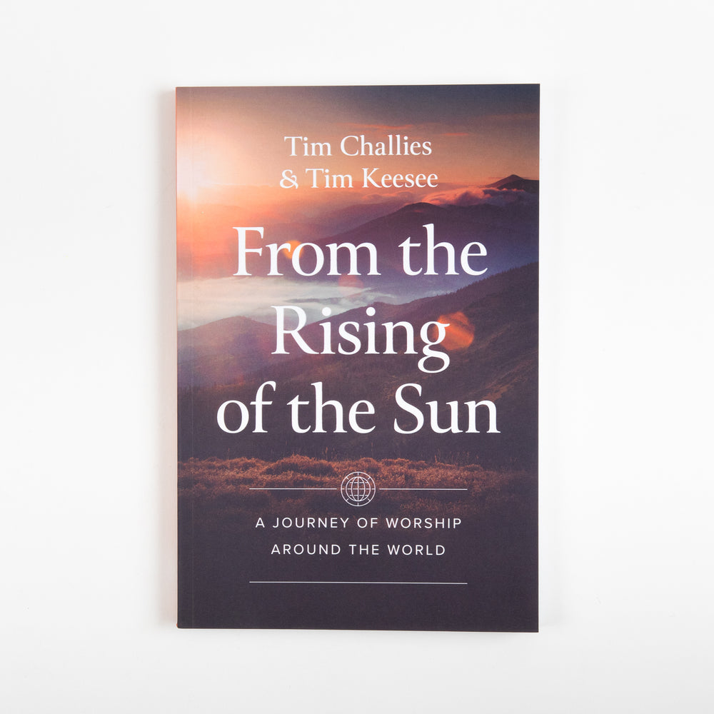 Front cover of 'From the Rising of the Sun: A Journey of Worship Around the World' by Tim Challies and Tim Keesee, featuring sunrise light over misty mountain ridges behind the white title text and a globe icon above the subtitle.