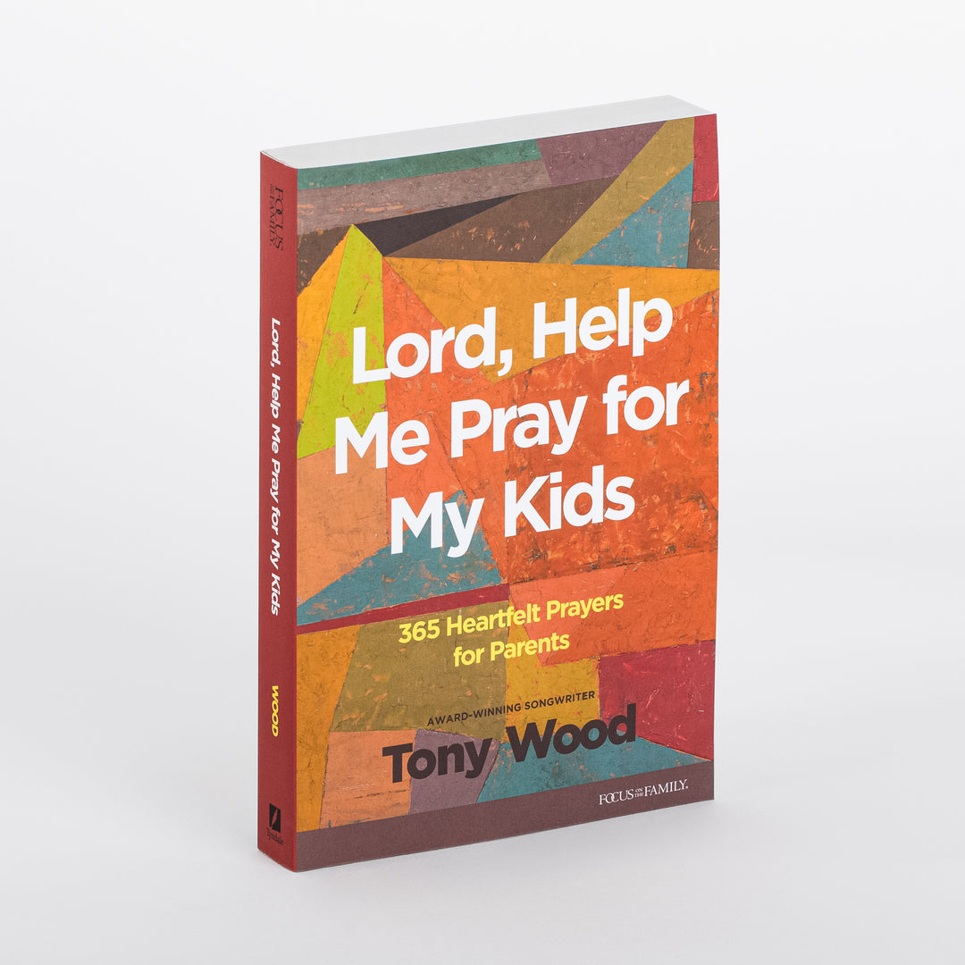 Angled 3/4 view of the paperback book Lord, Help Me Pray for My Kids: 365 Heartfelt Prayers for Parents by Tony Wood, showing both the front cover and spine. The cover is a geometric mosaic of orange, yellow, teal, olive, maroon, and brown triangles. White title text and yellow subtitle '365 Heartfelt Prayers for Parents' appear over the orange center, with the author name and a Focus on the Family logo below.