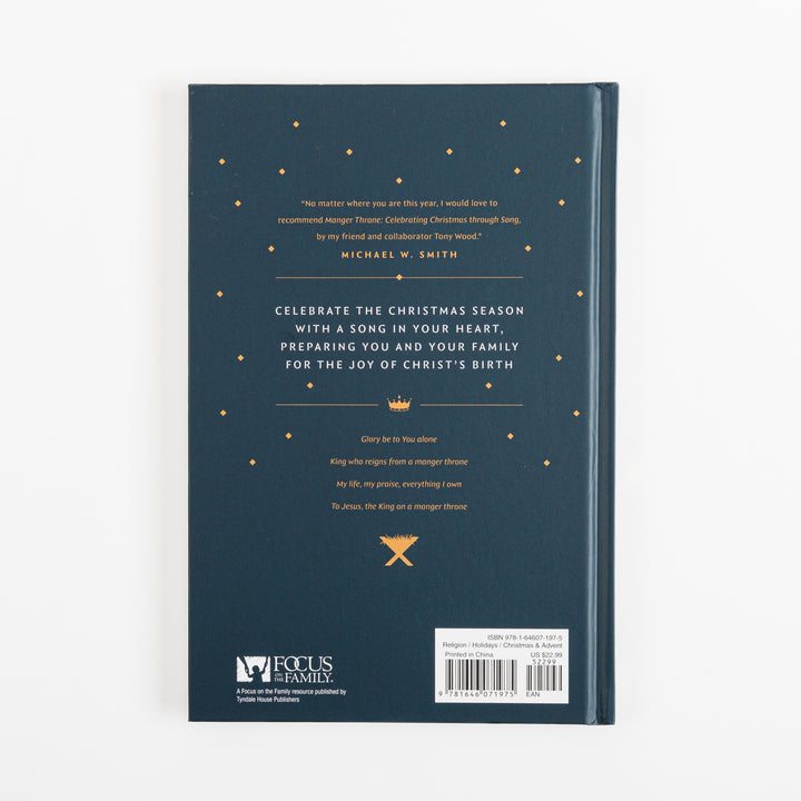 Back cover of the navy "Manger Throne" hardcover book with a gold star pattern, a review quote from Michael W. Smith, descriptive copy about celebrating Christmas with song, a short devotional verse, a gold crown-and-manger icon, the Focus on the Family logo, and the ISBN barcode.
