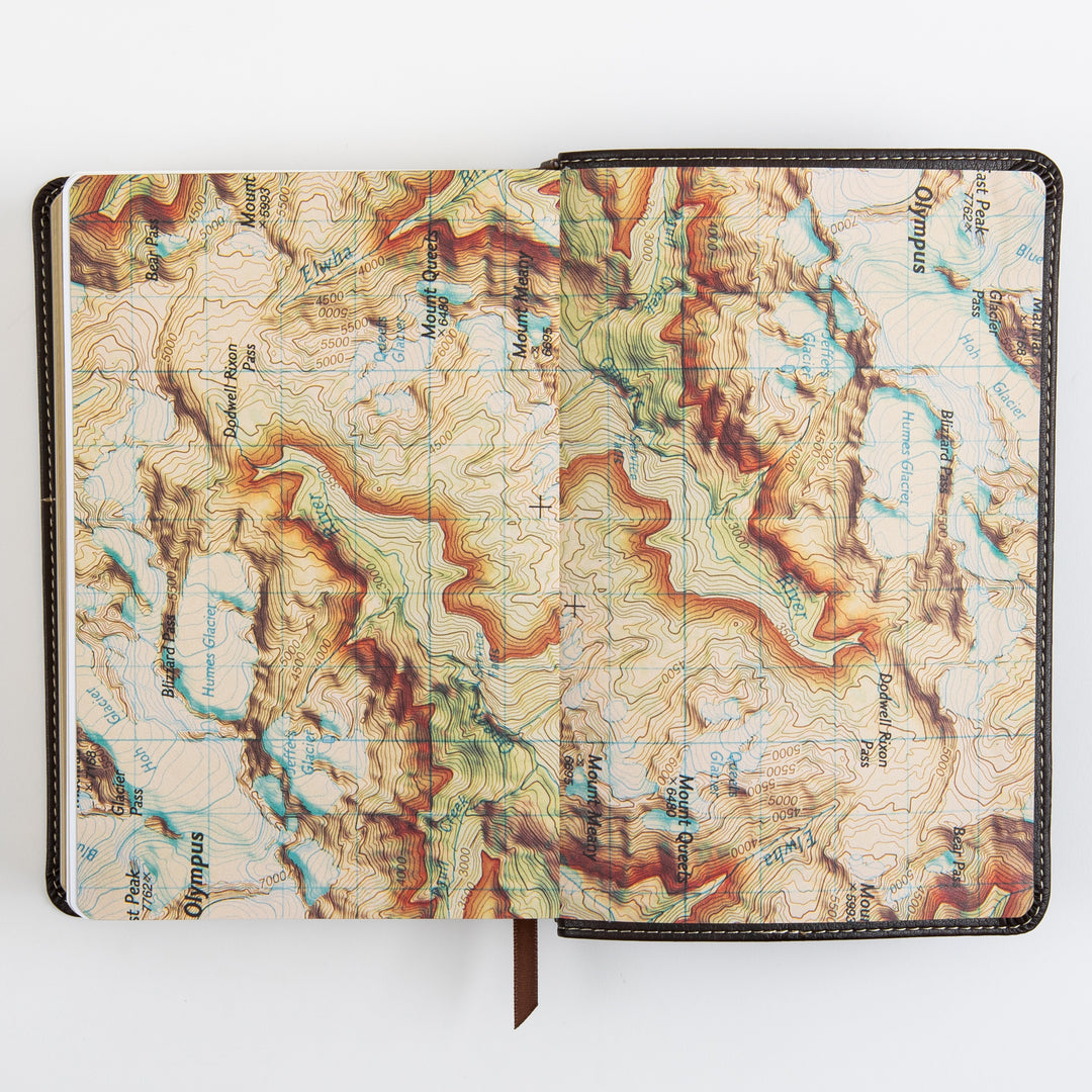 Open Bible page spread displaying a full two-page illustrated topographic map with contour lines, labeled mountain peaks, passes, and glaciers, part of the Explorer Edition&