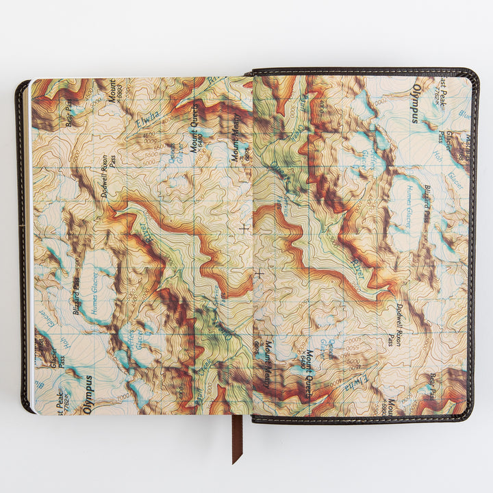 Open Bible page spread displaying a full two-page illustrated topographic map with contour lines, labeled mountain peaks, passes, and glaciers, part of the Explorer Edition&