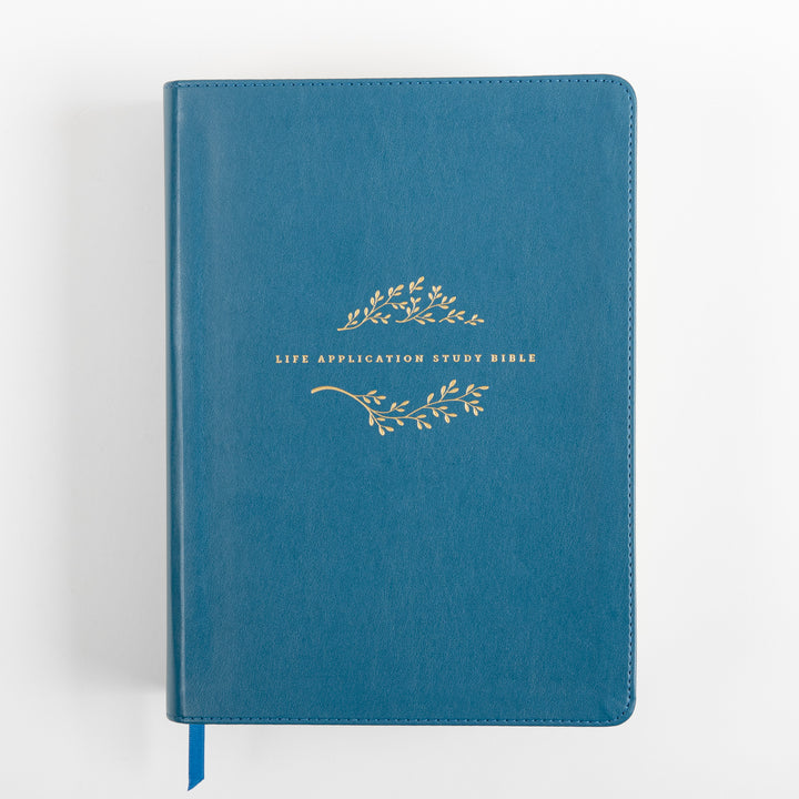Front cover of the teal leatherlike NLT Life Application Study Bible lying flat, with gold vine-and-leaf embossing framing the title &