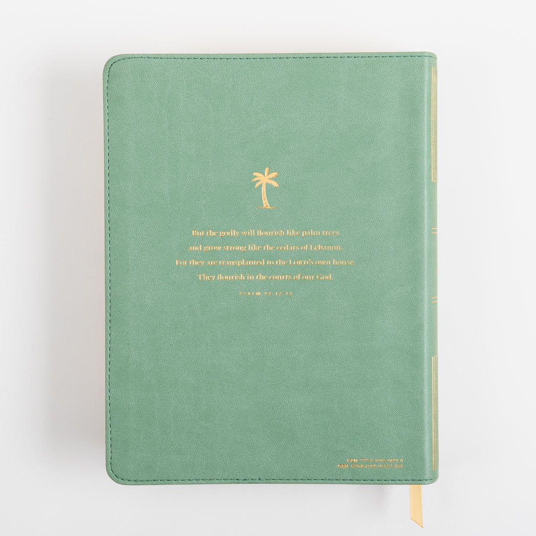 Back cover of the NLT Wide Margin Bible lying flat in sage green leatherlike, featuring a gold foil palm tree icon above gold foil text of Psalm 92:12-13 about the godly flourishing like palm trees, with a tan ribbon marker at the bottom edge.