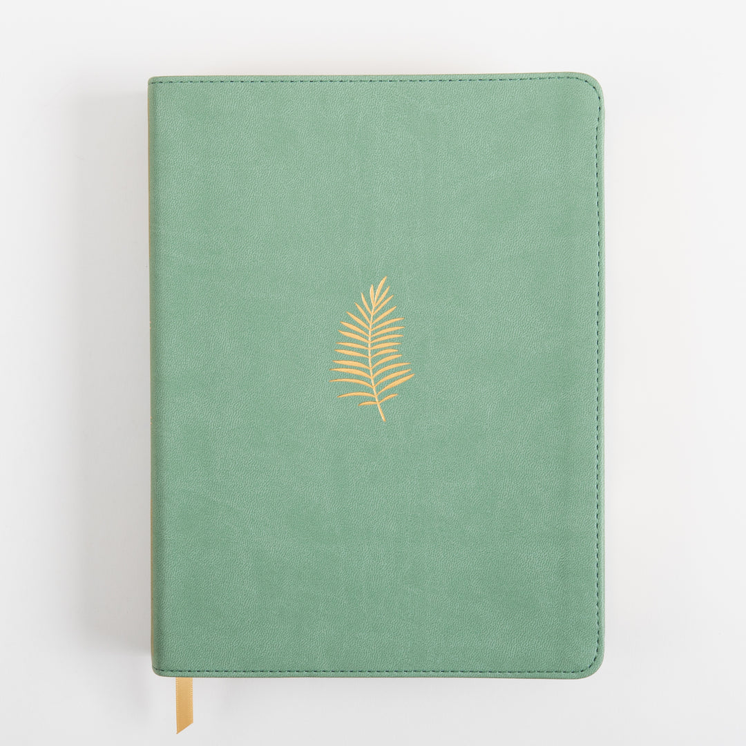 Front cover of the NLT Wide Margin Bible lying flat, in sage green leatherlike material with a small gold foil palm frond stamped in the center and a tan ribbon marker extending from the bottom edge.