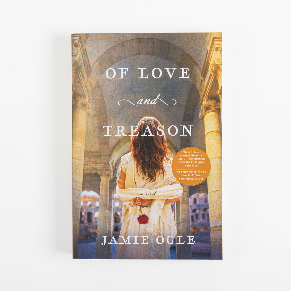 Front cover of the paperback novel "Of Love and Treason" by Jamie Ogle, shown flat and straight-on. A woman with long, wavy dark hair stands with her back to the camera, wearing a draped cream toga dress with a red rose held behind her, framed by stone columns and a vaulted archway overlooking sunlit ancient Roman buildings. The title is in white serif capitals with a cursive "and," an orange circular review-quote badge sits near the right edge, and the author's name appears at the bottom.