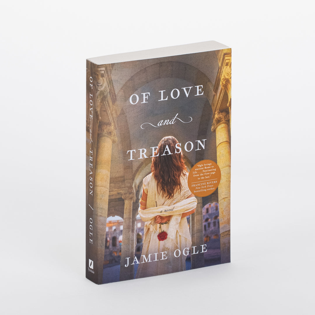 Paperback novel "Of Love and Treason" by Jamie Ogle, shown at a three-quarter angle revealing the front cover and spine. The art shows a woman with long, dark hair seen from behind, wearing a flowing cream toga dress with a red rose tucked at her waist, standing under a colonnaded stone archway overlooking a golden-lit ancient Roman street. The title appears in white serif capitals with a cursive "and," plus an orange review-quote badge at right. The spine repeats the title and author name.