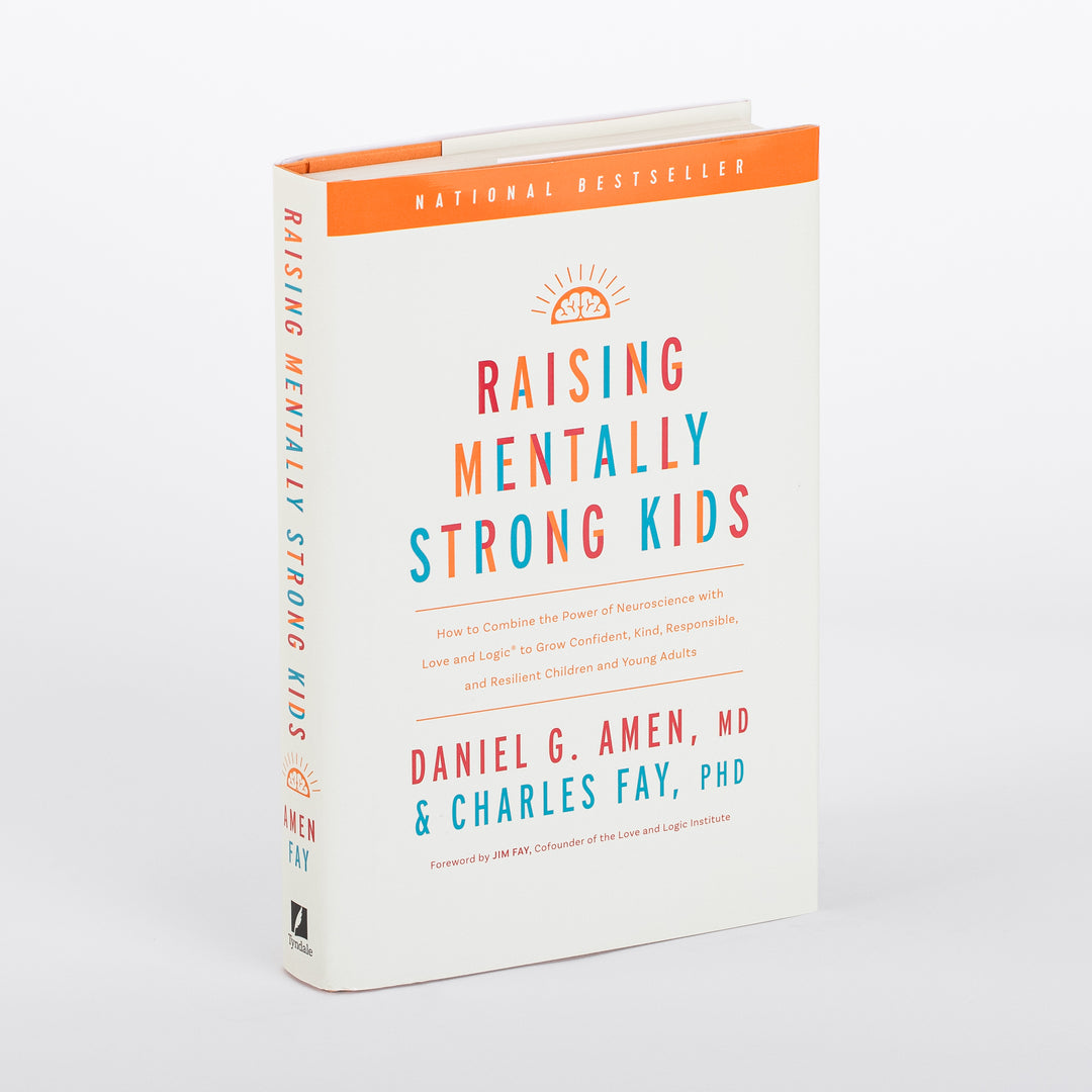Hardcover book photographed at an angle showing both the front cover and spine of Raising Mentally Strong Kids by Daniel G. Amen, MD and Charles Fay, PhD, foreword by Jim Fay. Cream-colored cover with an orange National Bestseller banner across the top, an orange sunrise-over-brain icon, and the title in bold multicolor letters (orange, teal, and red). The spine repeats the title vertically in the same colors with a Tyndale logo at the base.