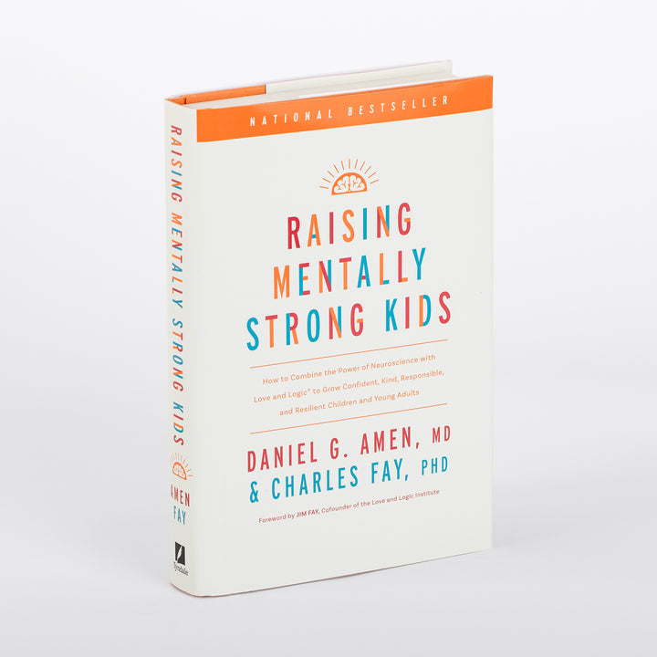 Hardcover book photographed at an angle showing both the front cover and spine of Raising Mentally Strong Kids by Daniel G. Amen, MD and Charles Fay, PhD, foreword by Jim Fay. Cream-colored cover with an orange National Bestseller banner across the top, an orange sunrise-over-brain icon, and the title in bold multicolor letters (orange, teal, and red). The spine repeats the title vertically in the same colors with a Tyndale logo at the base.