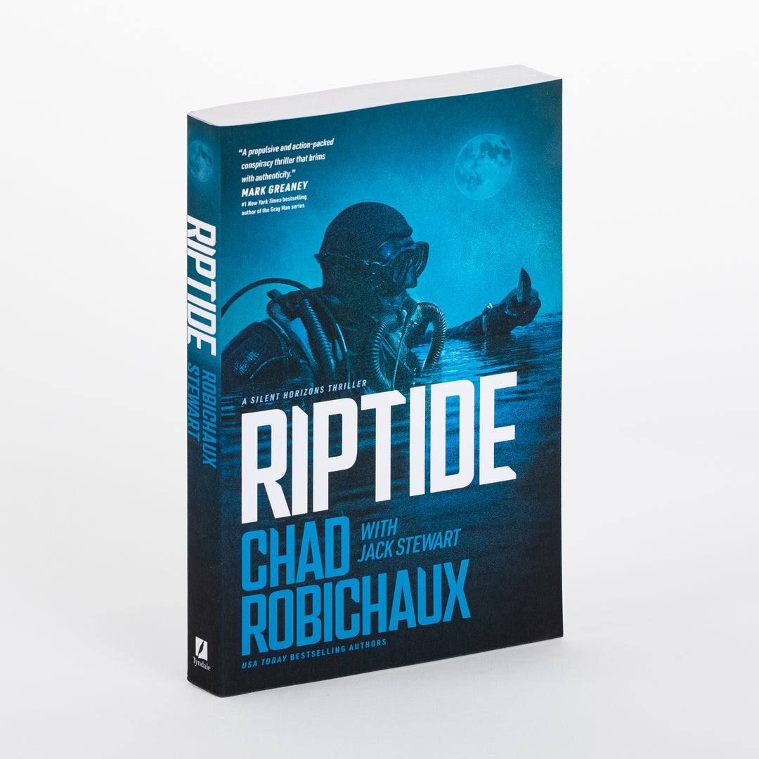 3D mockup of the paperback 'Riptide: A Silent Horizons Novel' by Chad Robichaux with Jack Stewart, angled to show the front cover and spine. Dark teal-blue nighttime scene: a masked tactical diver surfaces under a full moon, a hand reaching up beside him. A blurb quote sits near the top; 'RIPTIDE' appears in large white/blue block letters below 'A SILENT HORIZONS THRILLER,' with the authors' names and 'USA TODAY BESTSELLING AUTHORS' beneath, on a plain gray background.