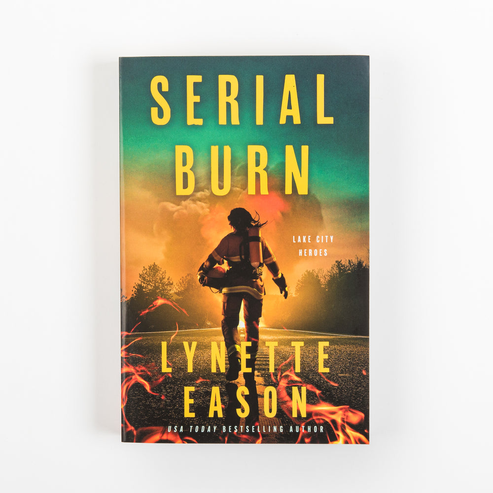 Front cover of the paperback 'Serial Burn' by Lynette Eason: a silhouetted firefighter in helmet and gear walking down a road toward smoke and orange flames under a teal-green night sky, with yellow title text and a 'Lake City Heroes' label.