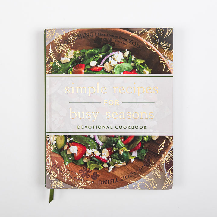 Front cover of Simple Recipes for Busy Seasons Devotional Cookbook, a hardcover with gold foil title text on a cream band, framed above and below by a photo of a spinach salad with strawberries, feta, and almonds in a wooden bowl, with gold leaf line-art illustrations.