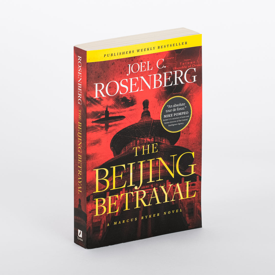 Paperback book of The Beijing Betrayal by Joel C. Rosenberg standing at an angle, showing both the front cover and spine against a white background. The cover art is a dramatic red-and-black silhouette of Beijing's Temple of Heaven with a submarine cutting through water beneath a faint map showing Taiwan. A yellow banner reads "Publishers Weekly Bestseller," with a circular badge quoting Mike Pompeo calling it "An absolute tour de force." Below the title is the tagline "A Marcus Ryker Novel."