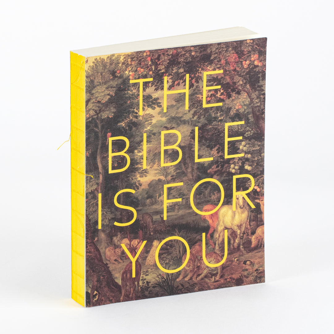 Softcover journal 'The Bible Is for You' angled to show its yellow-edged pages, with a cover featuring a lush painted forest scene of trees, deer, and other animals, overlaid with bold yellow capital letters spelling THE BIBLE IS FOR YOU.