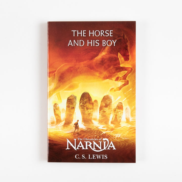 Front cover of The Horse and His Boy, book three of The Chronicles of Narnia by C.S. Lewis, showing a fiery orange desert scene with a running horse silhouette above ancient standing stones and a lone traveler.