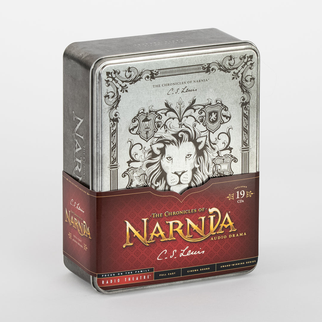 Angled view of The Chronicles of Narnia Radio Theatre Collector's Edition tin box, silver metal lid engraved with a lion's face framed by ornate scrollwork and family crests, wrapped in a red paper band reading 'The Chronicles of Narnia Audio Drama, C.S. Lewis' and noting 19 CDs included.