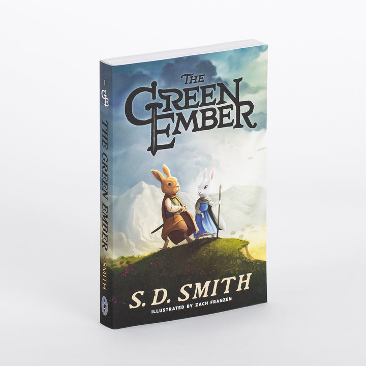 Angled view of The Green Ember paperback by S. D. Smith, showing the spine and front cover: two cloaked rabbits, one carrying a sword, standing on a grassy hilltop under a cloudy sky.