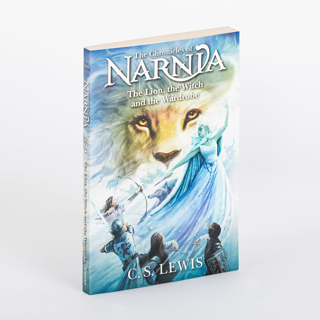 Paperback cover of The Chronicles of Narnia: The Lion, the Witch and the Wardrobe by C.S. Lewis, angled view, showing a lion's face, the White Witch in a flowing blue gown with arm raised, and four children below against a wintry blue sky.