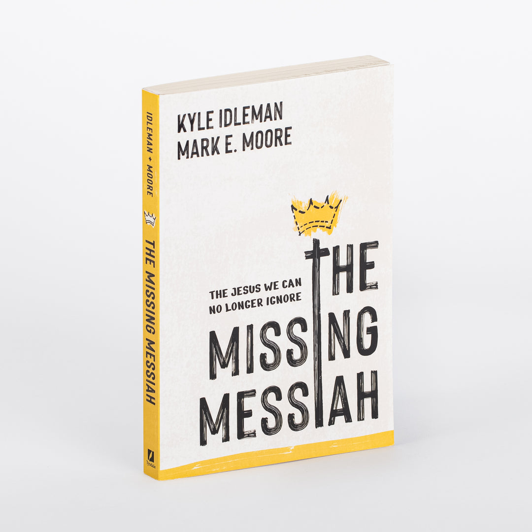 Paperback cover of 'The Missing Messiah: The Jesus We Can No Longer Ignore' by Kyle Idleman and Mark E. Moore, shown at a three-quarter angle so both the front cover and spine are visible. Cream background, hand-drawn yellow crown resting on a black cross that forms the letter I in 'MISSING,' bold black hand-lettered title, and a yellow stripe along the bottom edge and spine.