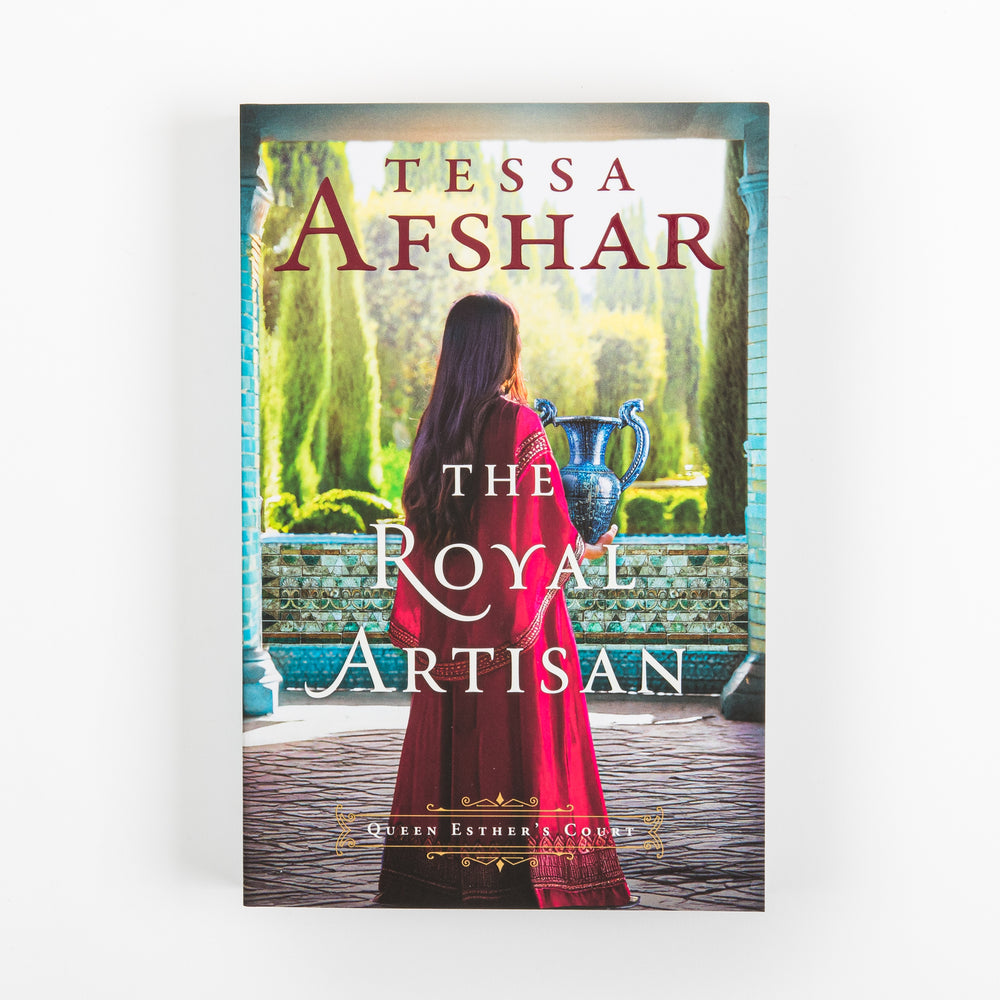 Front cover of The Royal Artisan by Tessa Afshar, shown straight-on. A woman in a red robe stands with her back to the viewer, holding a blue and silver vase, framed by a turquoise-tiled archway overlooking cypress trees and a garden courtyard. Queen Esther's Court series label above the bottom edge.