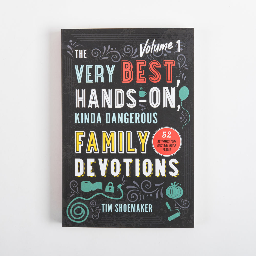 Front cover of 'The Very Best, Hands-On, Kinda Dangerous Family Devotions, Volume 1' by Tim Shoemaker, laid flat on white background: black cover with title in teal, red, and yellow lettering, a red circular badge reading '52 activities your kids will never forget,' and teal doodle icons of a balloon, toilet paper roll, lock, and pumpkin.
