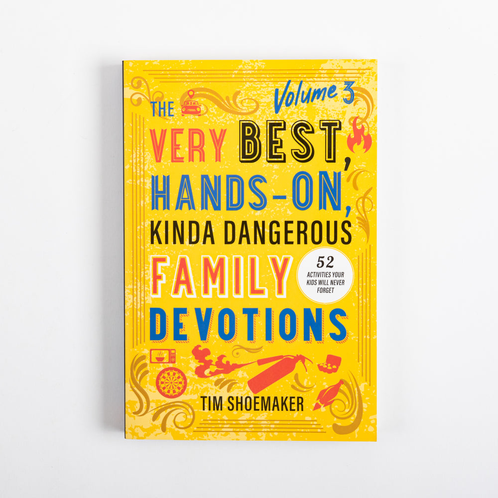 Front cover of 'The Very Best, Hands-On, Kinda Dangerous Family Devotions, Volume 3' by Tim Shoemaker, shown flat against a white background. Bright yellow cover with red, blue, and black hand-lettered title text, a white circular badge reading '52 Activities Your Kids Will Never Forget,' and illustrated icons of a school bus, flame, dart board, and spray can.